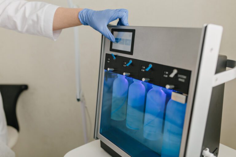 A person wearing a blue glove operates a touchscreen on a medical or laboratory device with several transparent bottles inside, utilizing advanced Oxygen & Filtration Technology.